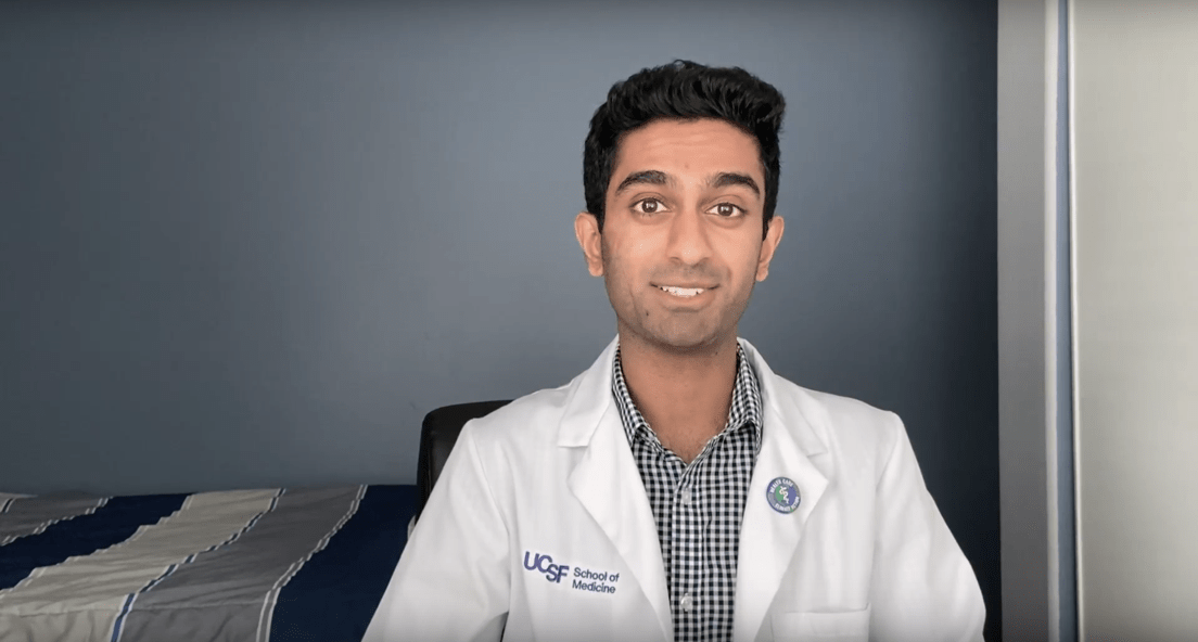 Photo of Raj in a white lab coat, seated against a gray wall.