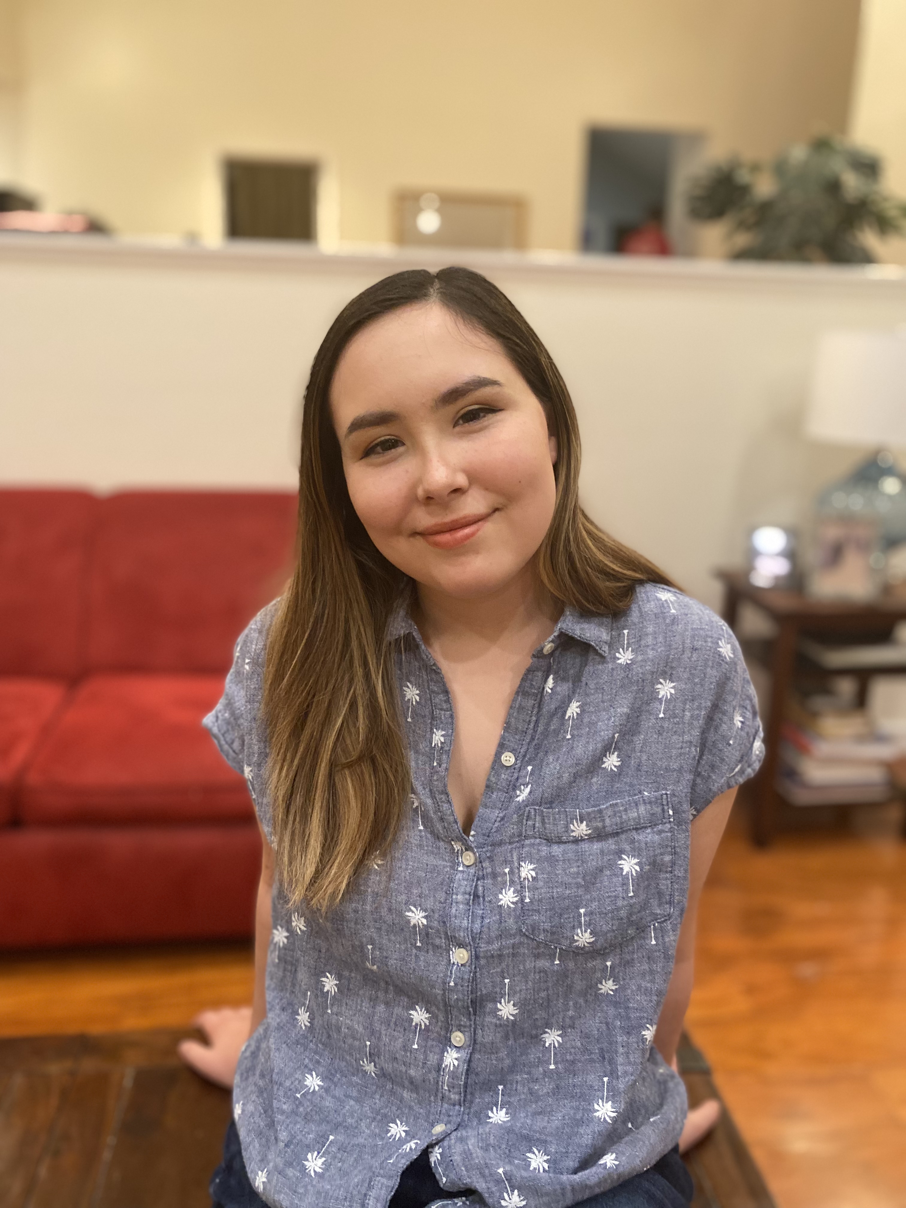 Photo of Rebekah leaning against a wooden table, wearing a blue, short-sleeved button-up top.