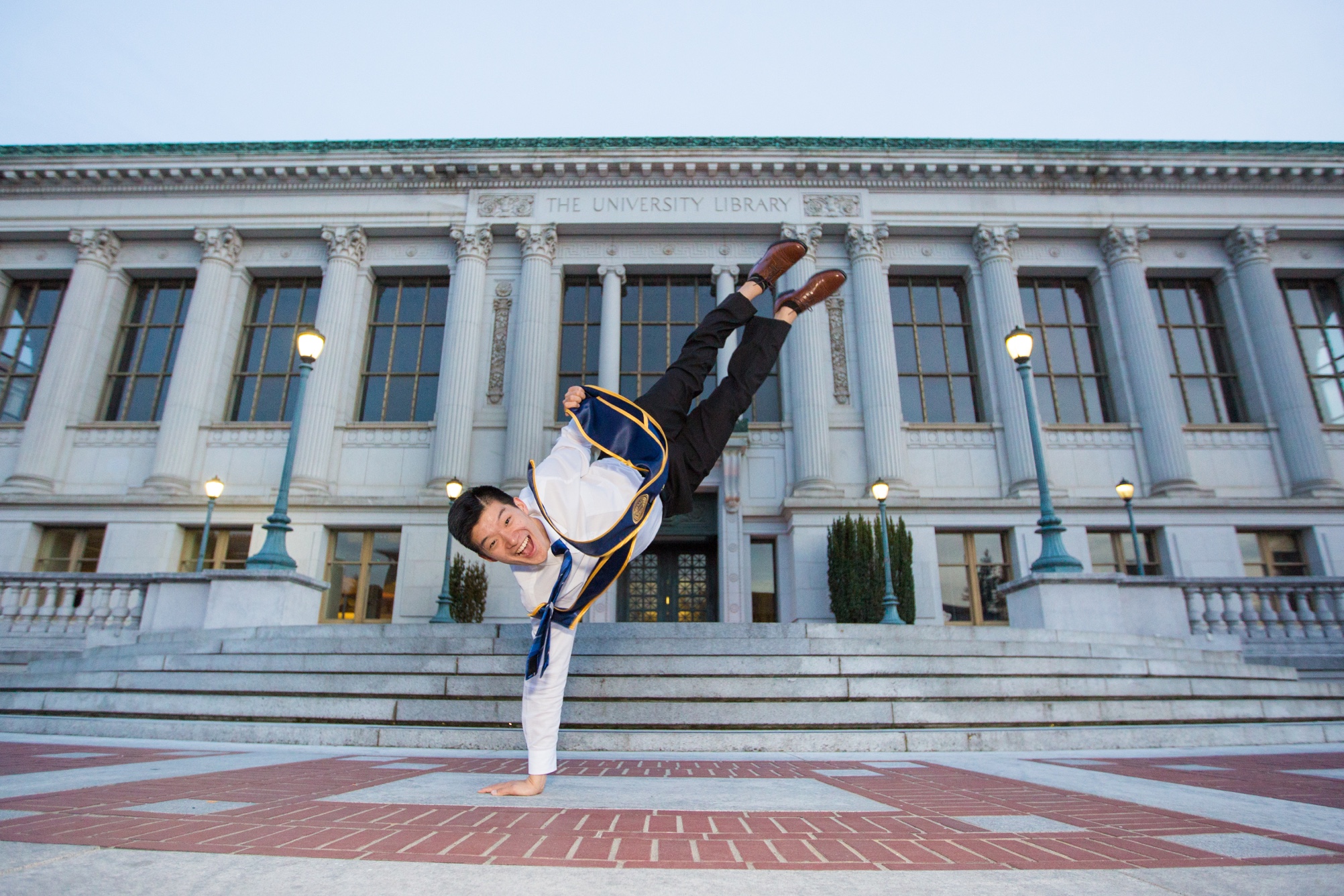 Photo of Robert in a one-handed handstand on the steps in front of Doe Library