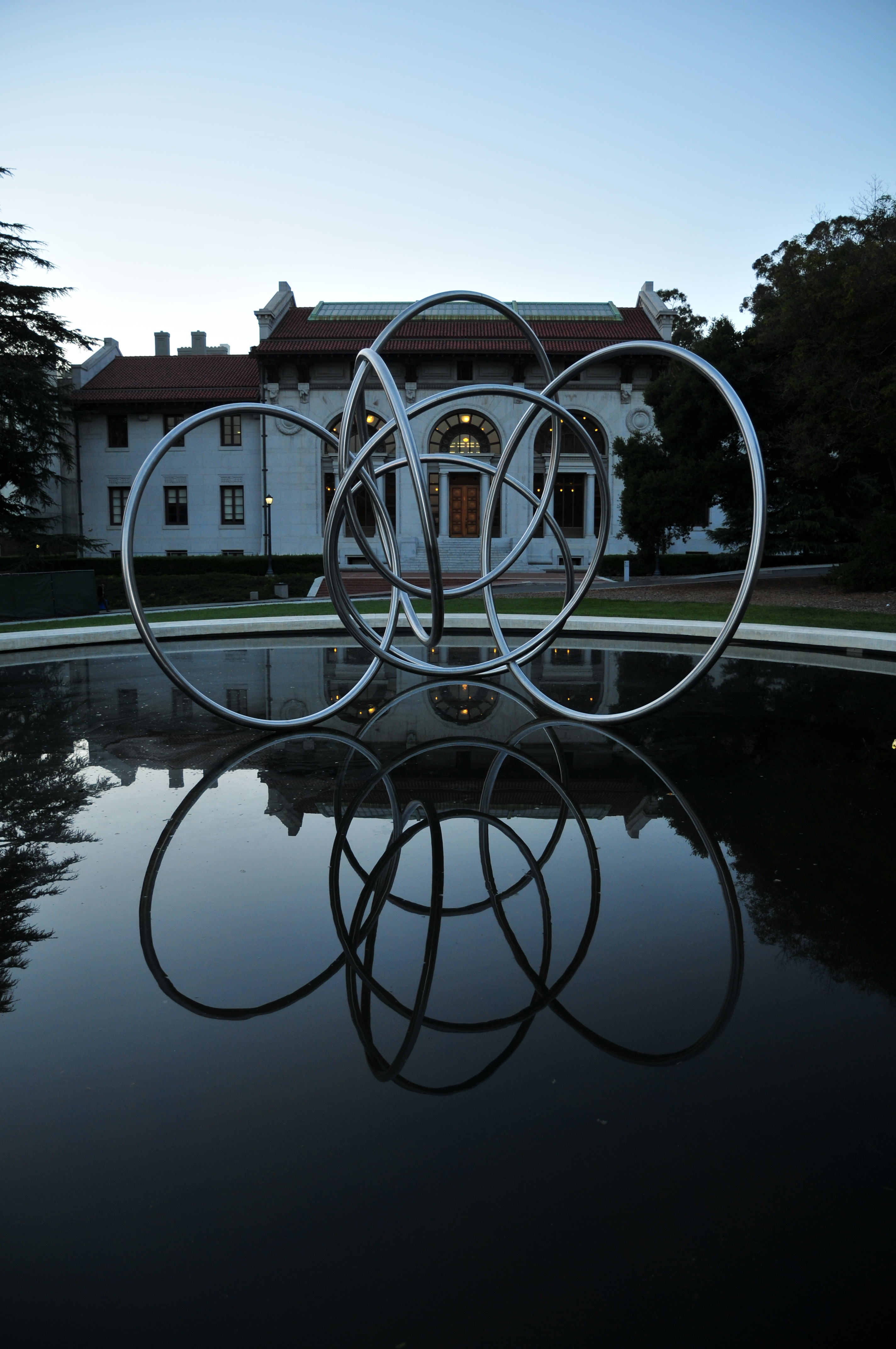 A photo shot at dusk of a sculpture of interlocking steel rings suspended above a pool in front of Hearst Memorial Mining Building.