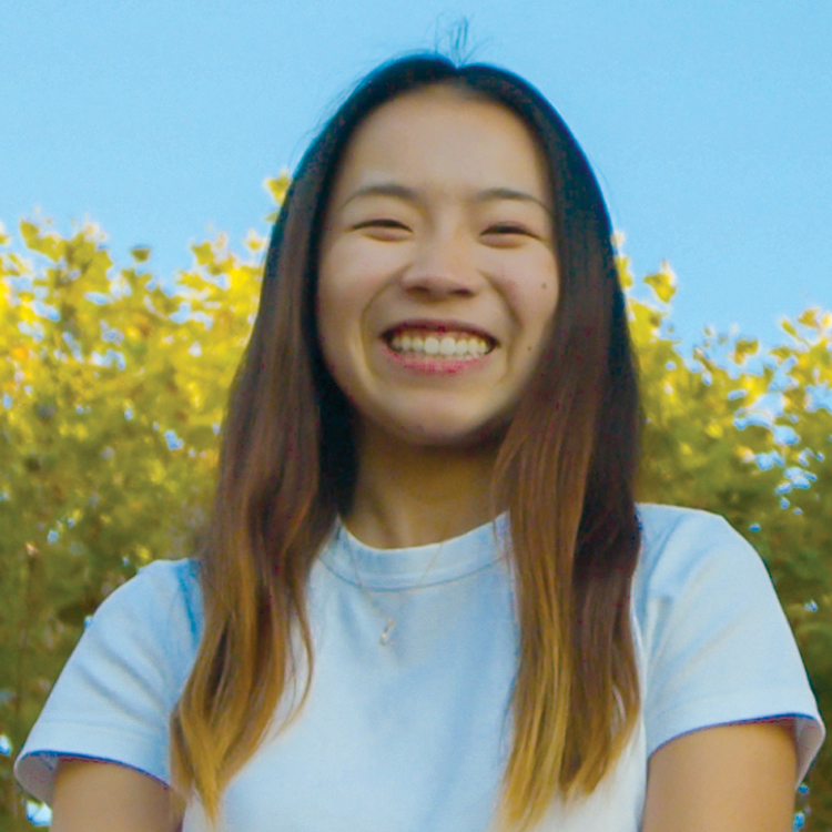 Photo of Sunny in a white shirt and blue jeans, sitting on steps with the Campanile behind her.