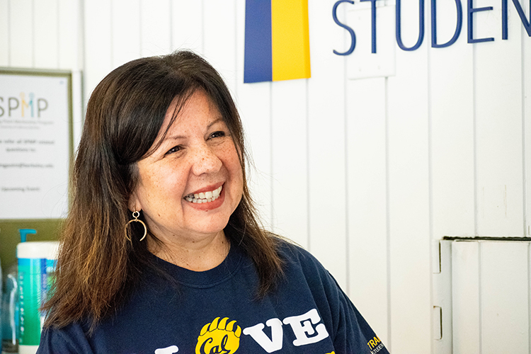 Photo of Lorena with long, brown hair, smiling, and wearing a blue and gold Cal shirt.