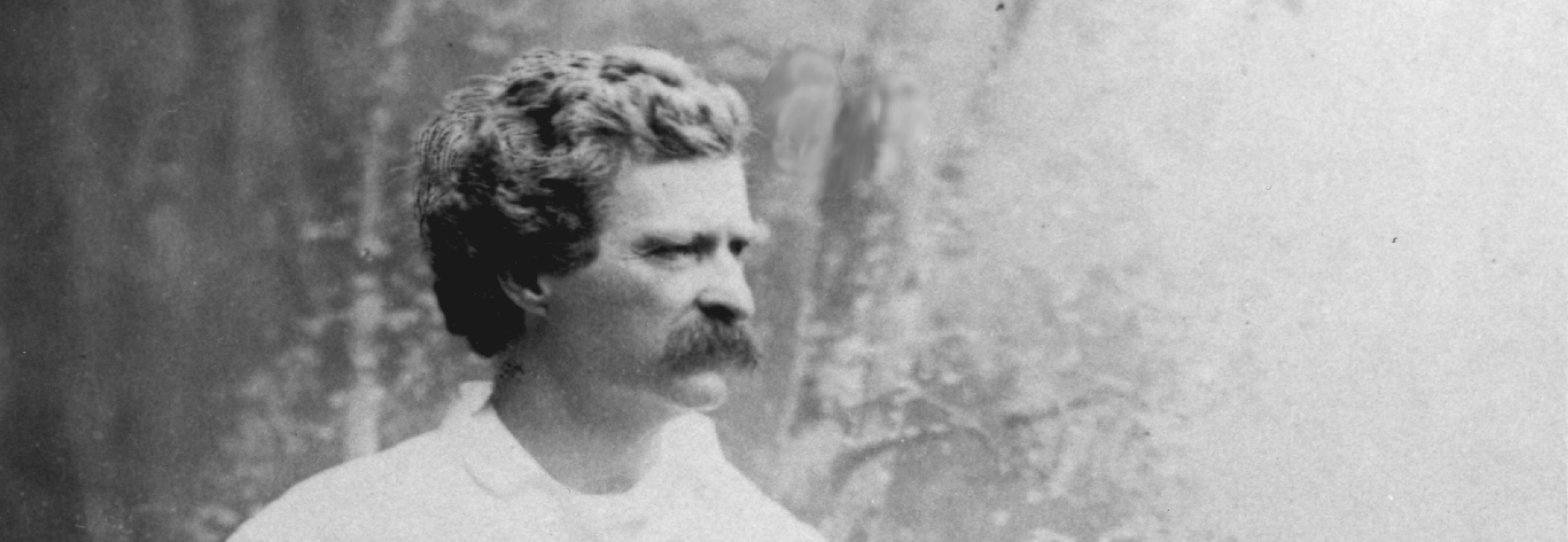 Black and white photo of Mark Twain with a copious mustache and white shirt looking off to the side