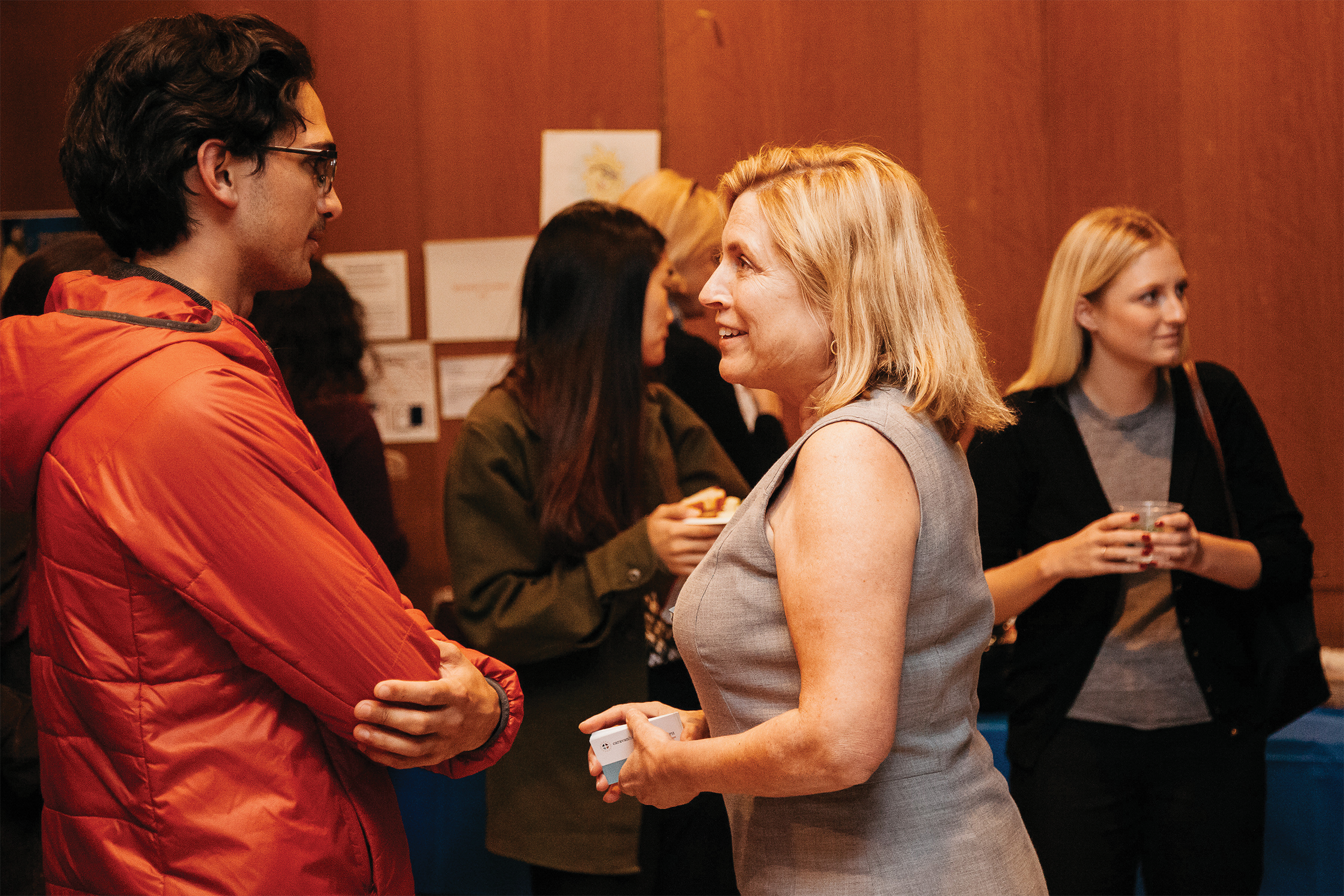 Photo of Lynn Barr M.P.H. ’10 in a grey dress talking to male student in an orange jacket.