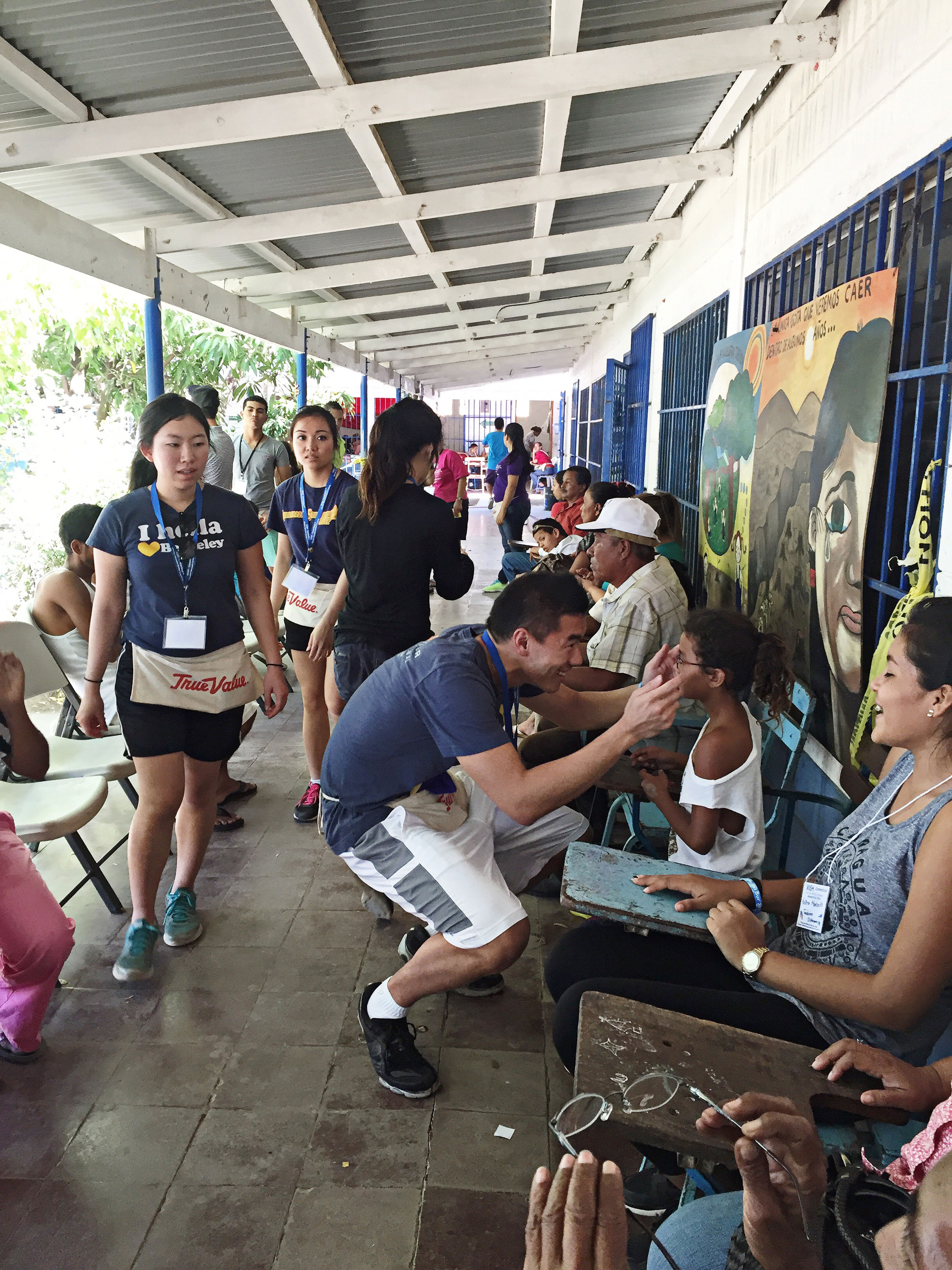 Photo of a Berkeley student checking that a child's glasses fit as community members look on.