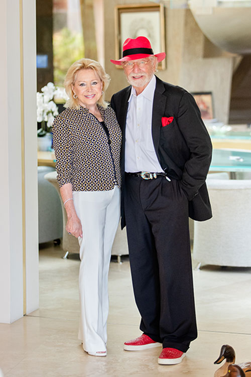 Photo of Nicole, wearing white pants and a diamond-patterned jacket, and Herbert, in his trademark red fedora.