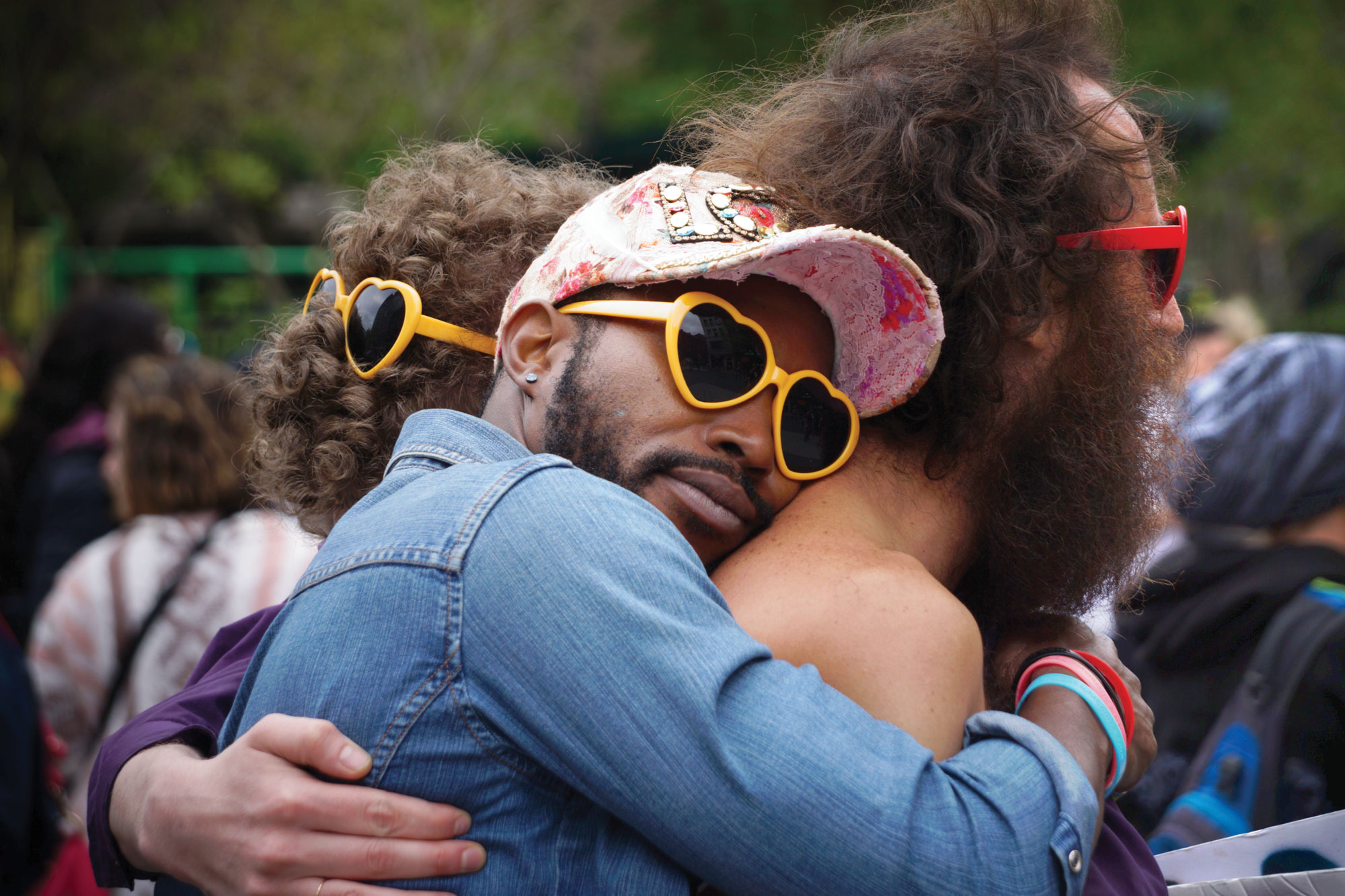 Photo of man wearing heart-shaped sunglasses hugging another man.