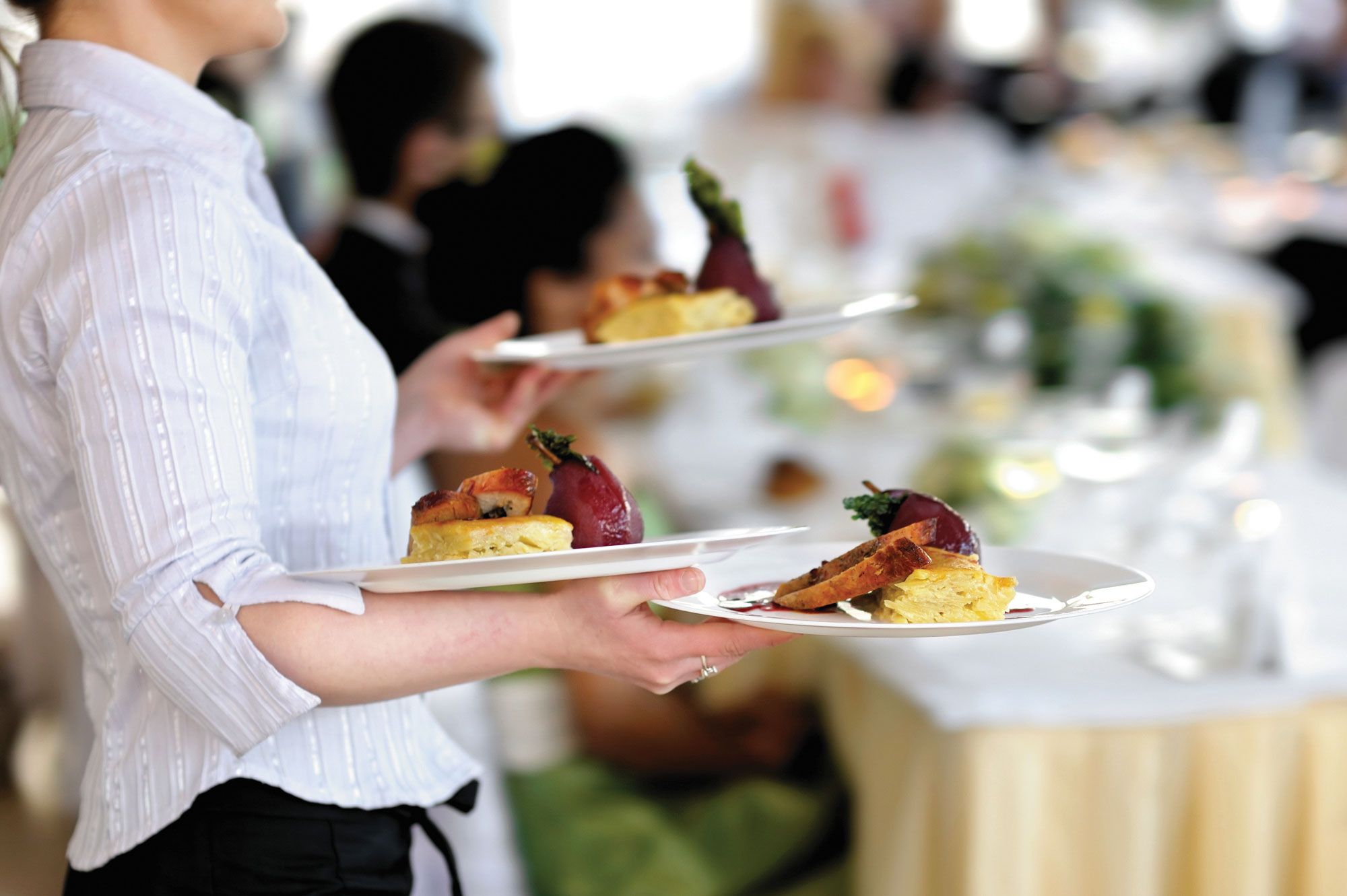 Photo of a waiter in a white shirt carrying three plates of food.