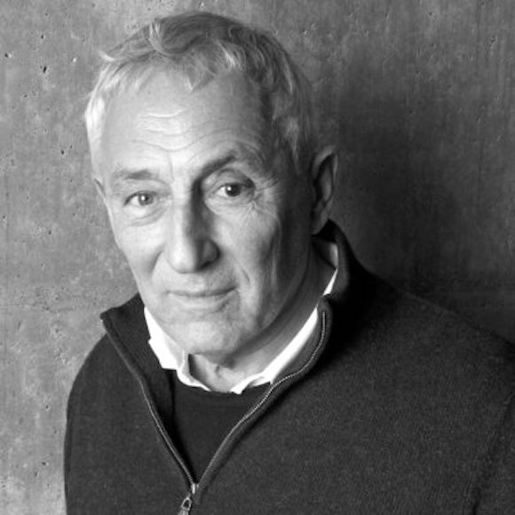 Black and white photo of a Ray standing against a textured wall in a dark sweater and jacket.