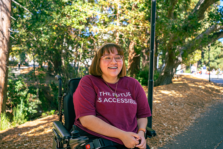 Photo of Mariana on a campus pathway wearing a t-shirt that says, 