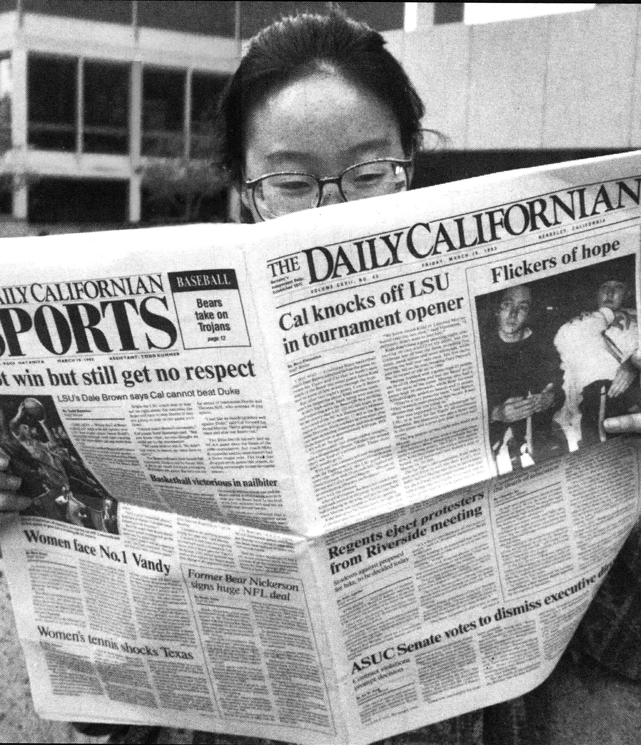 Black and white photo of a student poring over a copy of the newspaper.