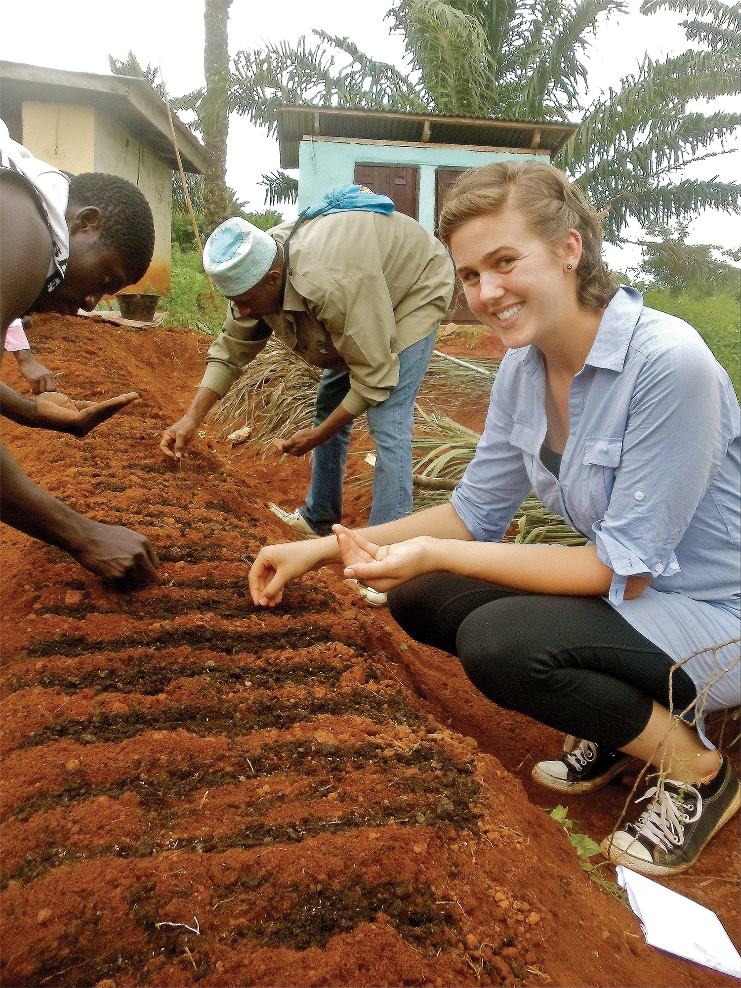 Photo of a young woman kneeling over a planting bed with three others in the background.