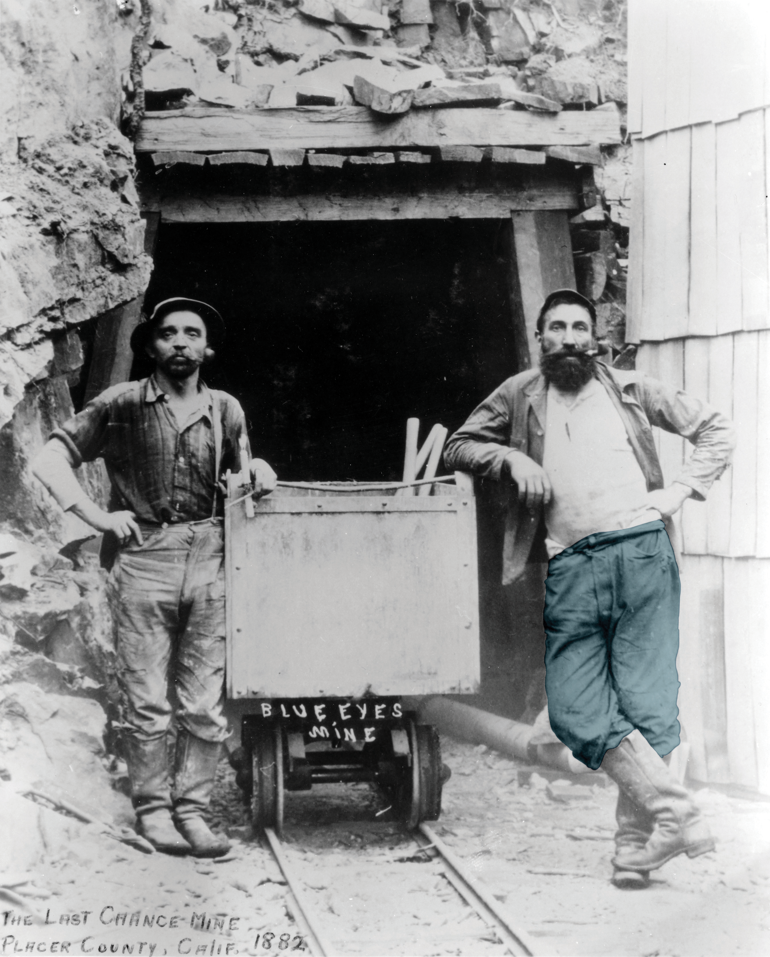 Black and white photo of two men standing outside a mine entrance leaning on a mine trolley.