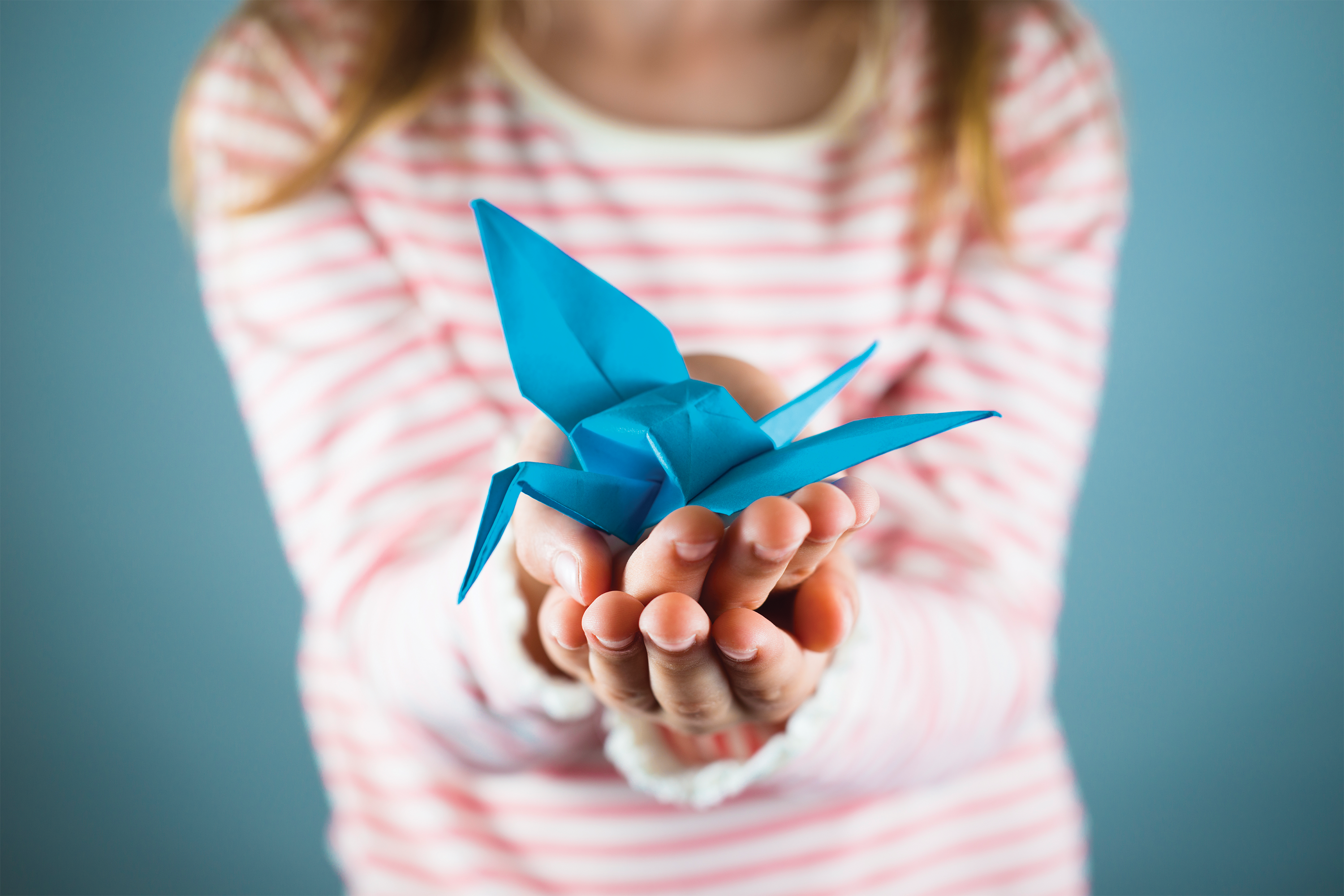 A photo of a young girl holding a blue origami bird.
