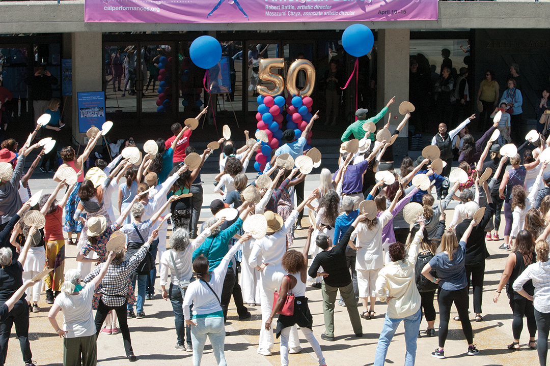 Photo of Alvin Ailey dancers and community members, most in white, with their right arms outstretched.