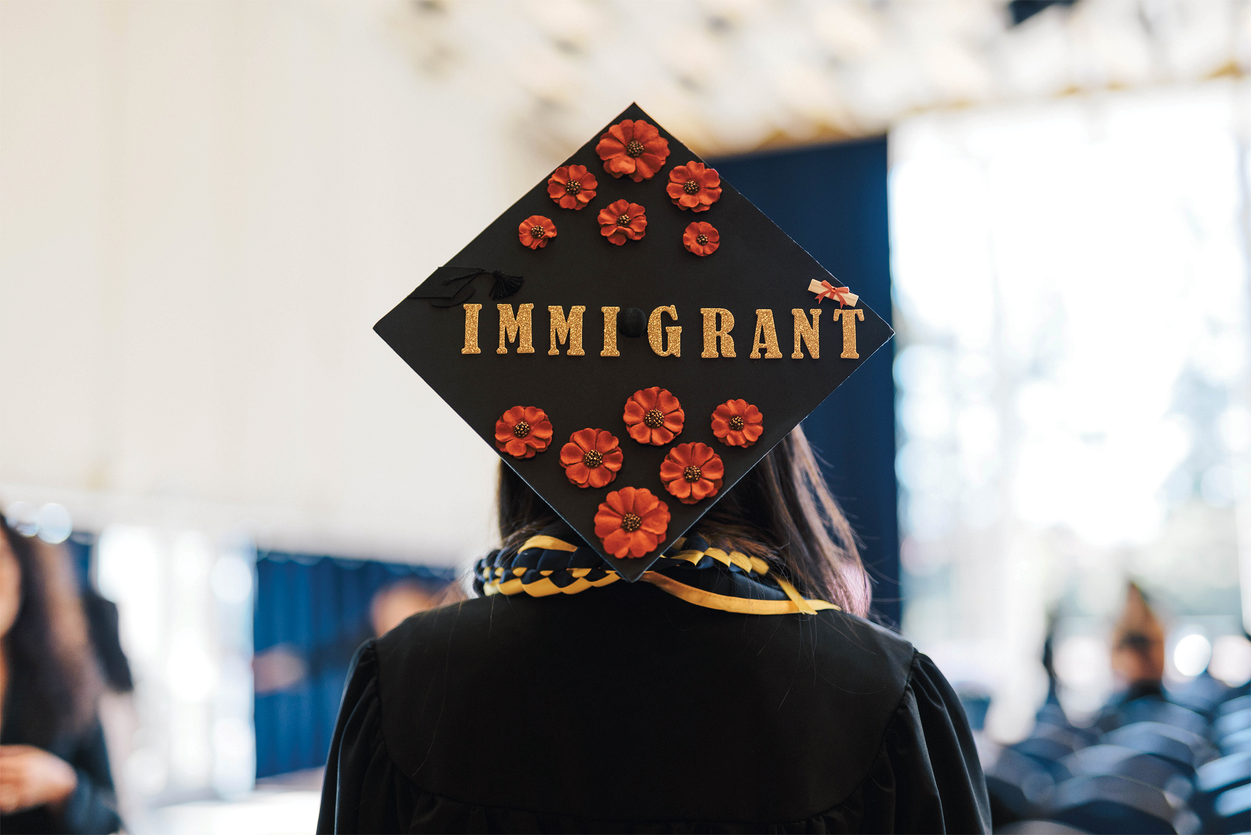 Photo of the back of a woman's cap, which has been decorated with flowers and the word, "Immigrant."