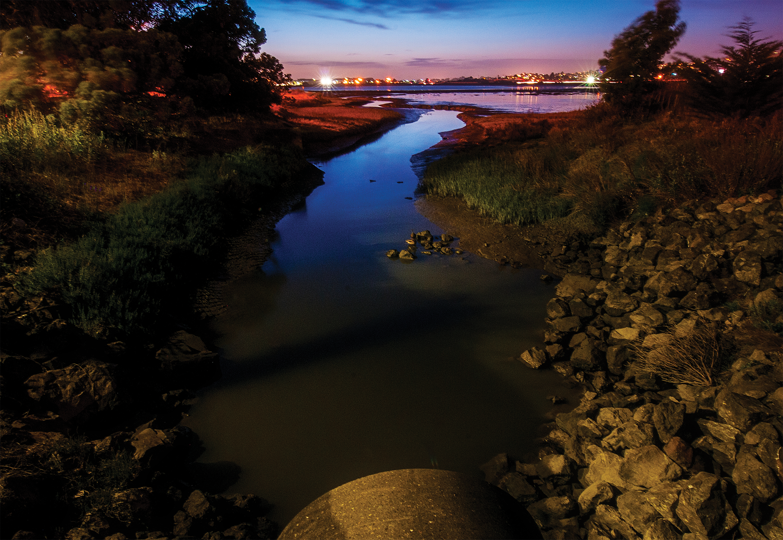 A moody photo in deep blues and earth tones of the San Francisco bay at night.