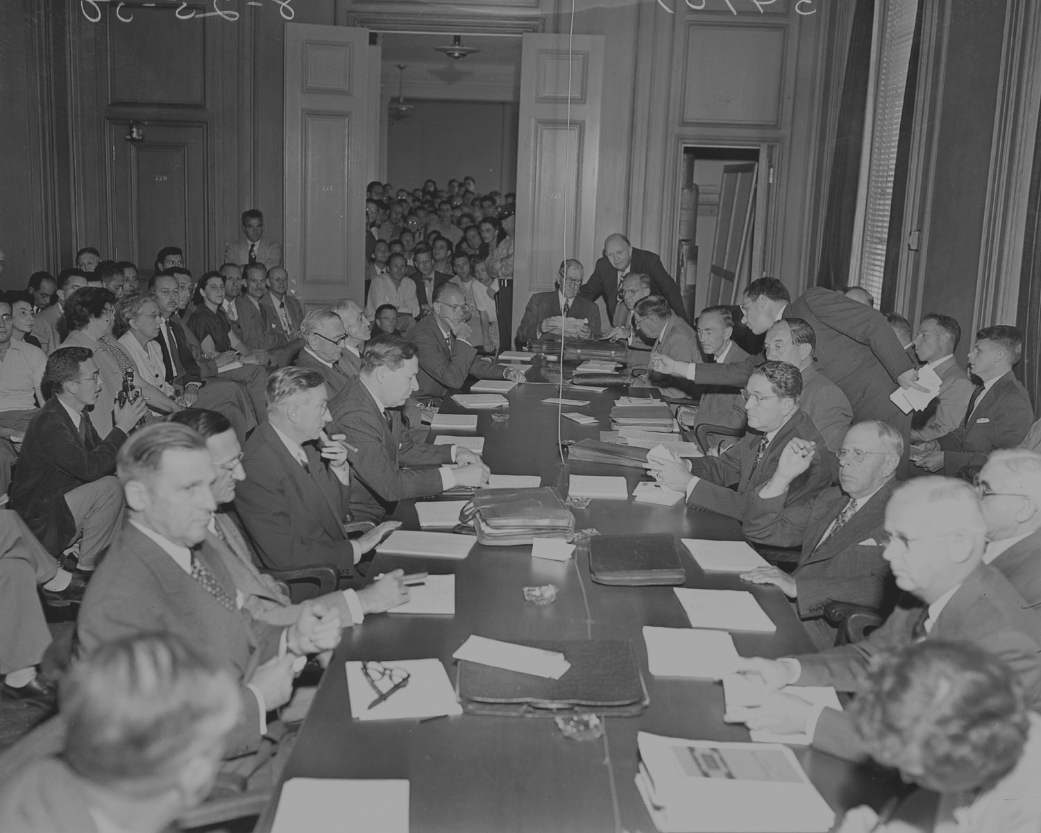 An historic photo of several people around a large table covered in papers.