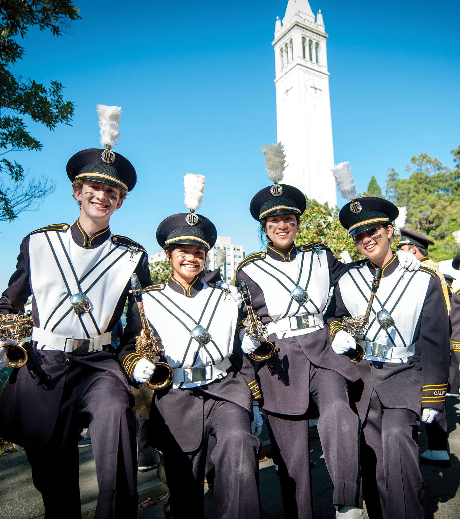 Photo of four women in their band uniforms kicking up a knee in front of the Campanile.