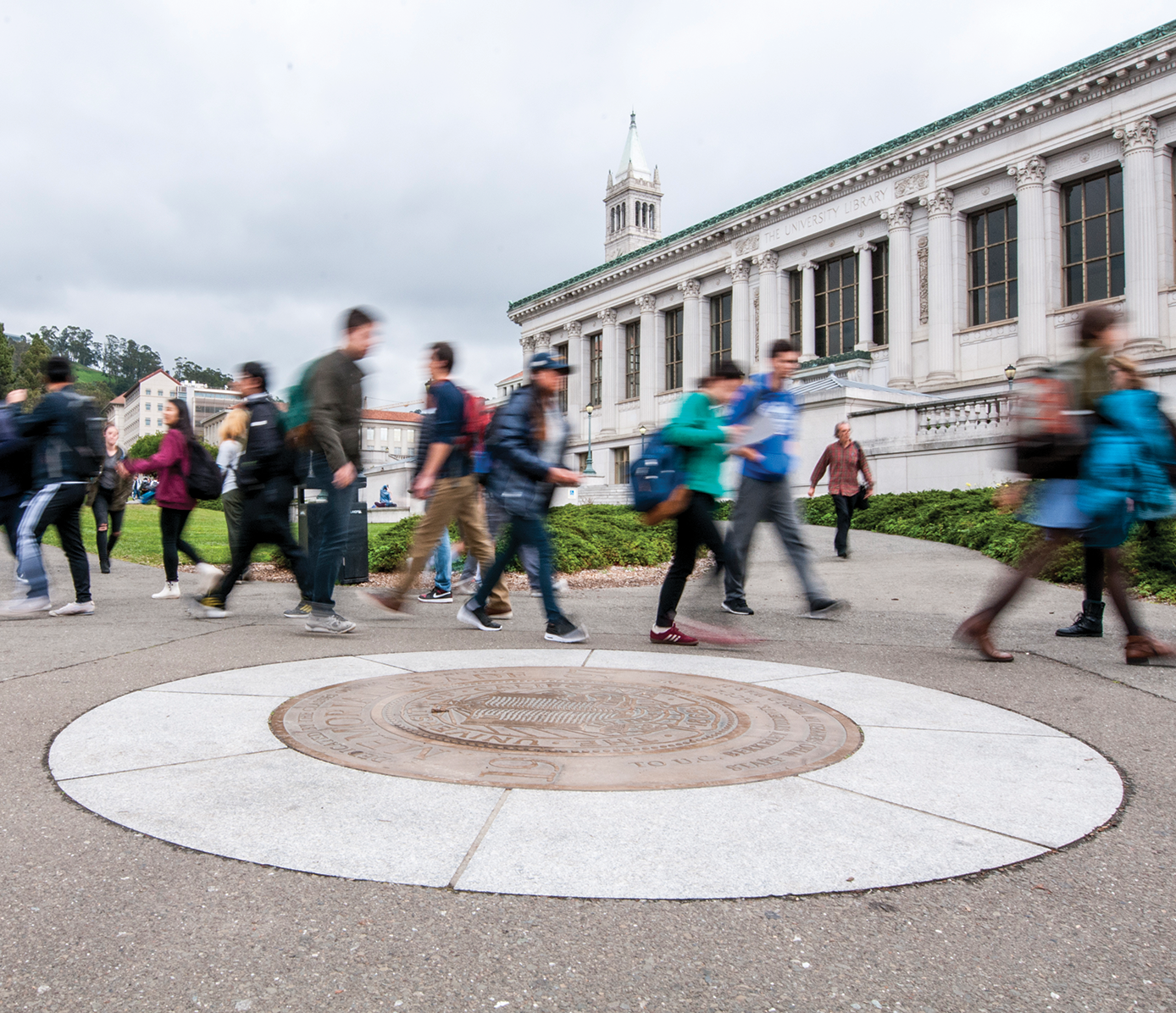 Photo of students rushing to class in front of Doe Library and stepping around the seal.