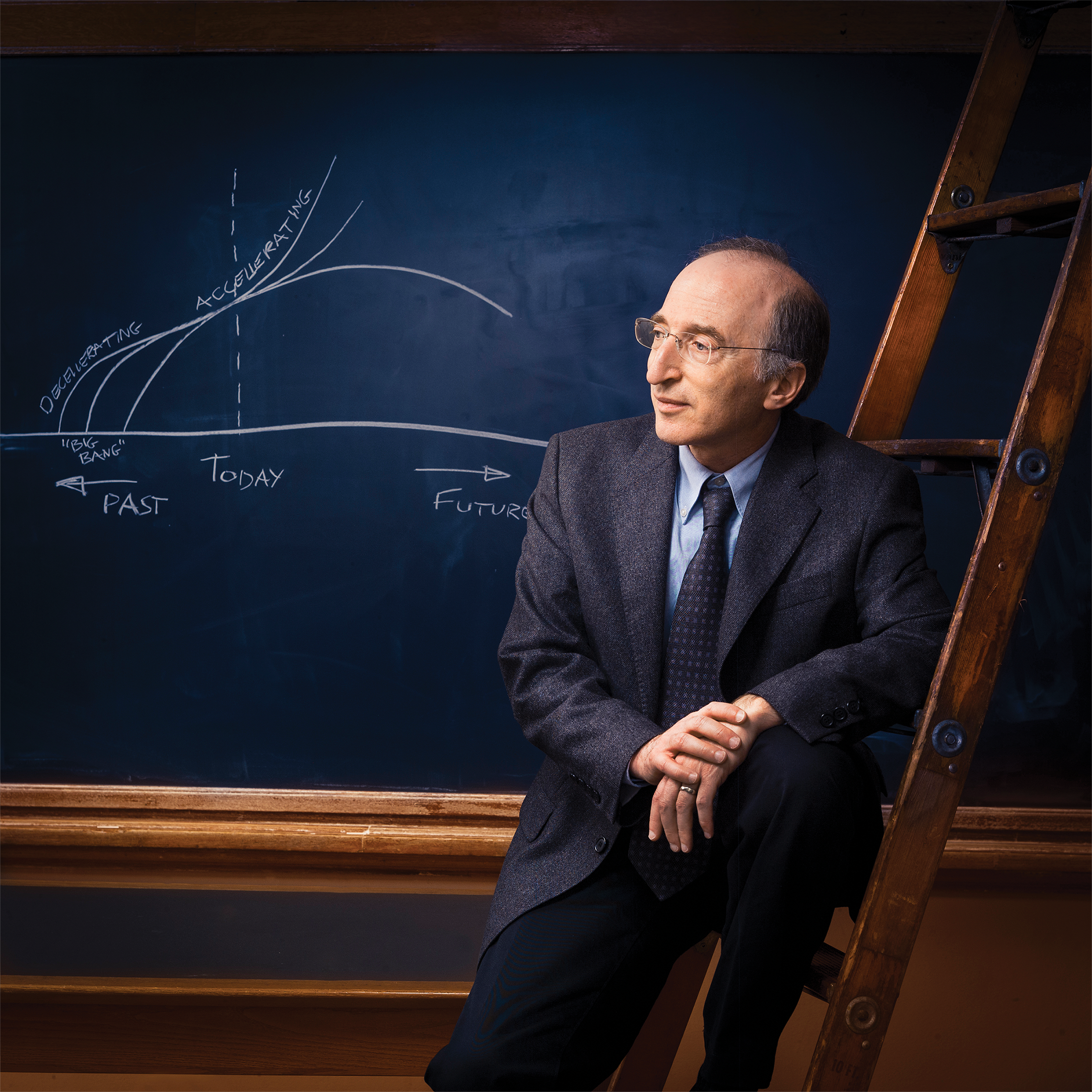 Photo of Saul Perlmutter perched on a ladder in front of a chalkboard.