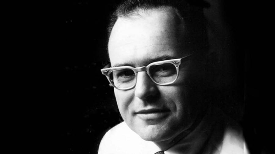 Black and white photo of Gordon against a black backdrop wearing a white shirt and glasses.