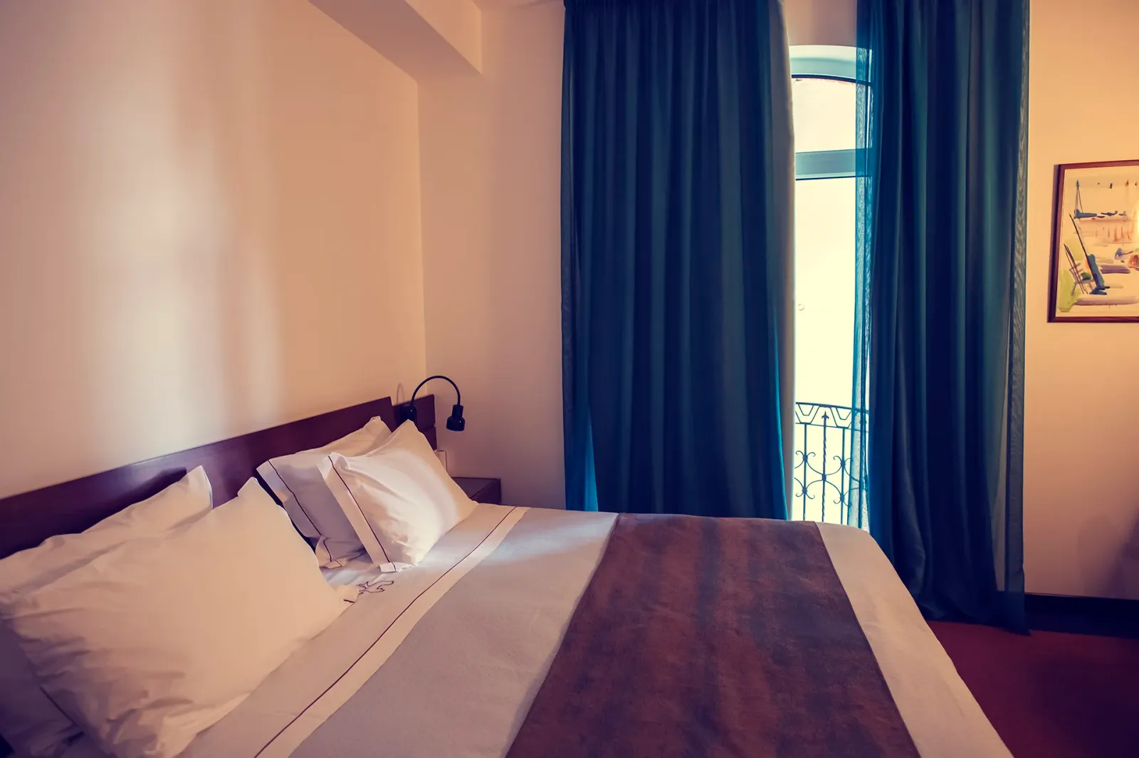 Camera d'albergo con letto rifatto, tende e balcone.