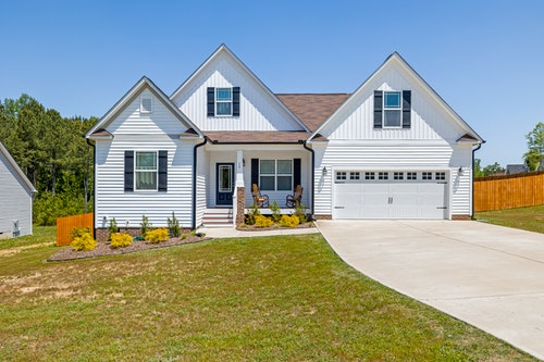 white house with black roof on lot with attached garage and driveway