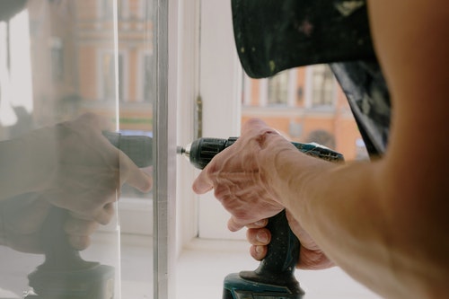 person using power drill to screw in bolt in window pane