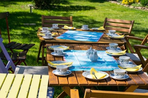 outdoor home entertaining table setting blue and yellow dishes and napkins on wooden table with seating