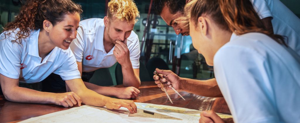 Four Sea Rangers hang over a sea chart, preparing an upcoming route.