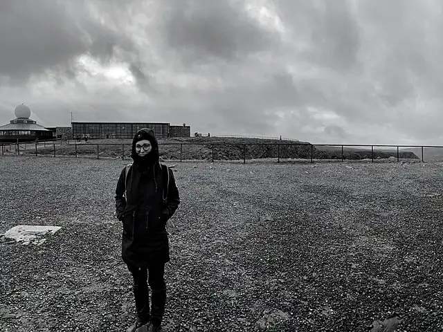 Schwarz-Weiß-Fotografie die Autorin in einem schwarzen Regenmantel mit Kapuze.