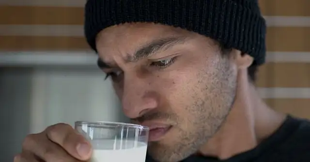 Chris Huriwai (ein junger Mann mit dunklen Augenbrauen, braunen Augen und einer schwarzen Strickmütze riecht mit fragendem Blick an einem Glas Milch, das er in seiner rechten Hand hält.