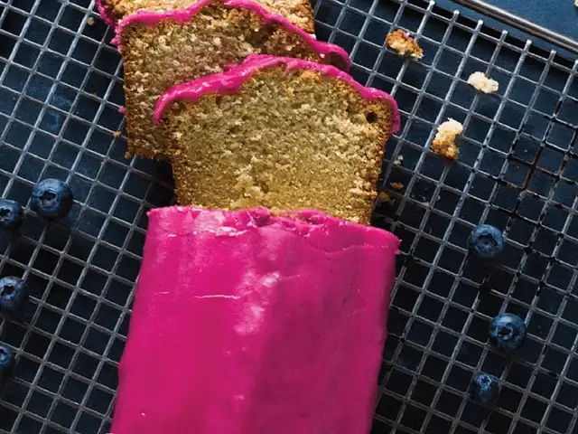 Zitronenkuchen mit Blaubeerguss von Lena Marie Radu – Foto von einem hellen, kastenförmigen Kuchen mit pinkem Zuckerguss auf einem Rost mit Heidelbeeren (Blaubeeren).)