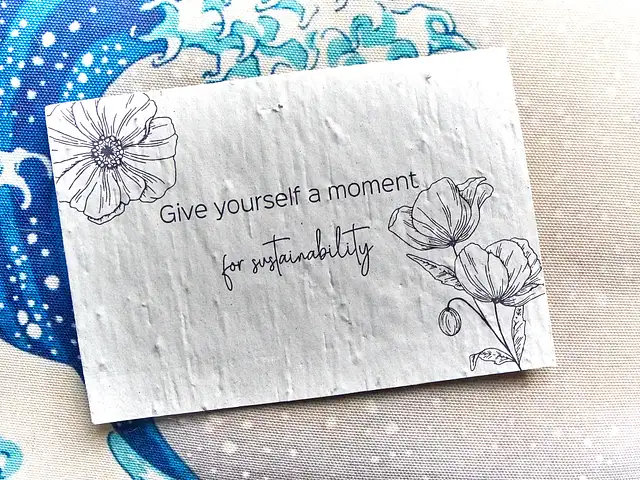 Eine cremefarbene Postkarte mit den Worten "Give yourself a moment for sustainability" liegt auf einem Kissen mit Wellenmotiv.