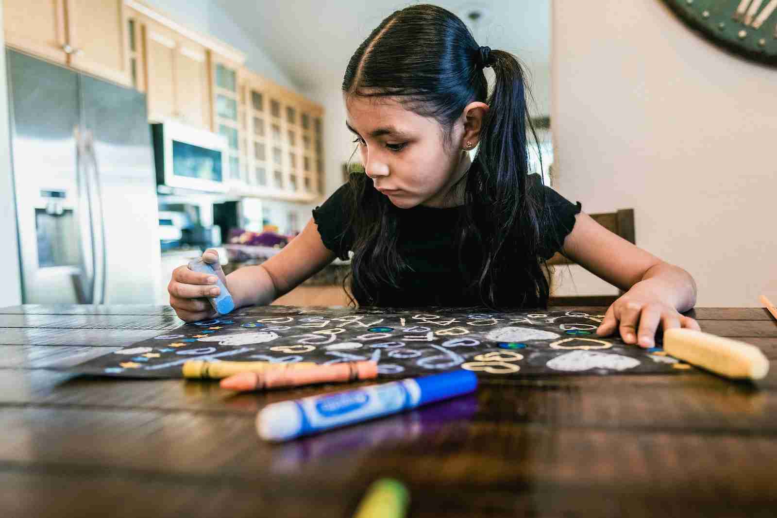 a little girl sitting at a table with crayons