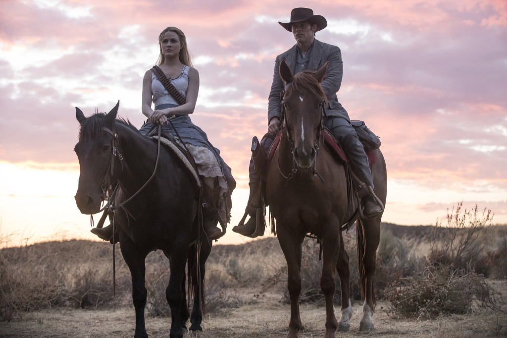 As the sun sets over the desert landscape, a man and a woman ride horses, creating a dynamic and adventurous scene. The woman, wearing a white dress and long blonde hair flowing in the wind, sits gracefully on her horse as they traverse the desert sands. A man in a cowboy hat exudes confidence as he sits atop his own horse, adding to the rugged and adventurous atmosphere. The woman holds a gun tightly, ready for any action that may come their way. The image captures the spirit of freedom and exploration in the desert.