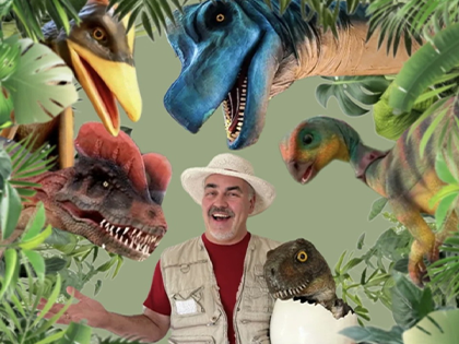 Performer in explorer costume surrounded by realistic dinosaur puppets, promoting a family dinosaur show