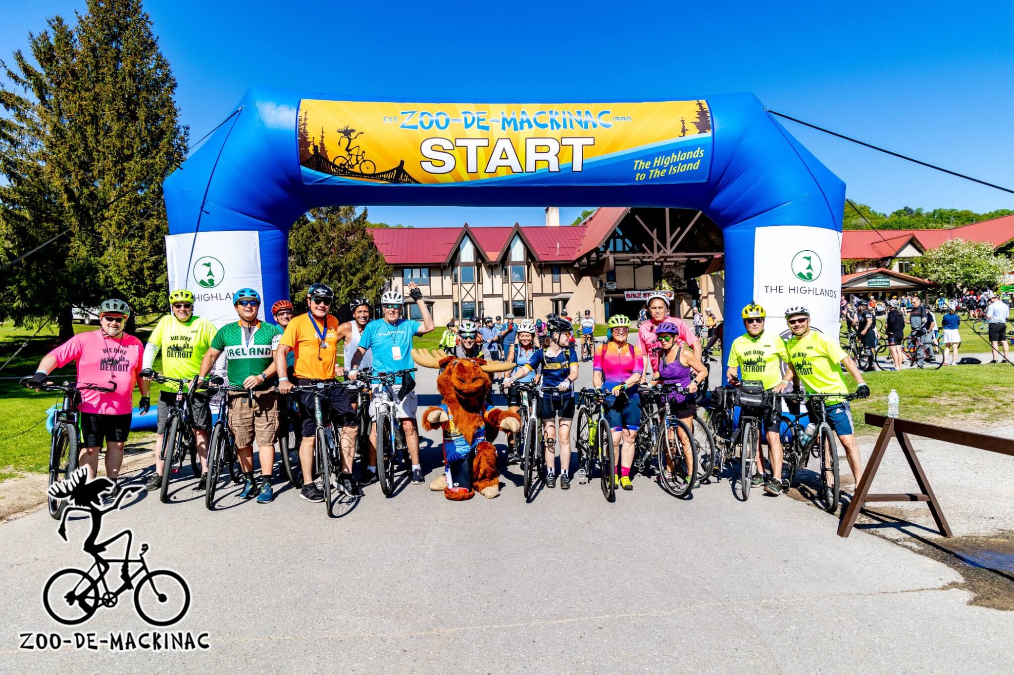 Zoo-De-Mackinac START arch at The Highlands with cyclists and moose mascot. Est. 1990 — The Highlands to The Island.