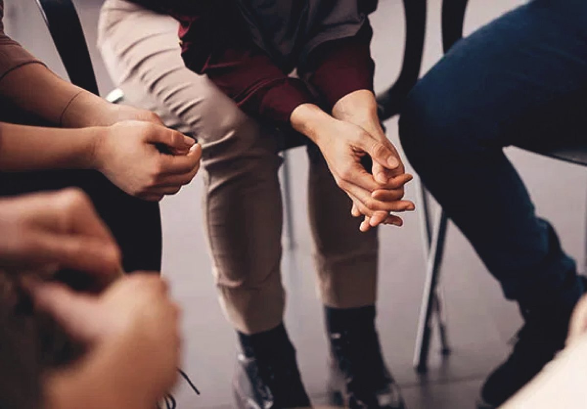 Support group members sit in a circle with clasped hands during an Alcoholics Anonymous (AA) meeting