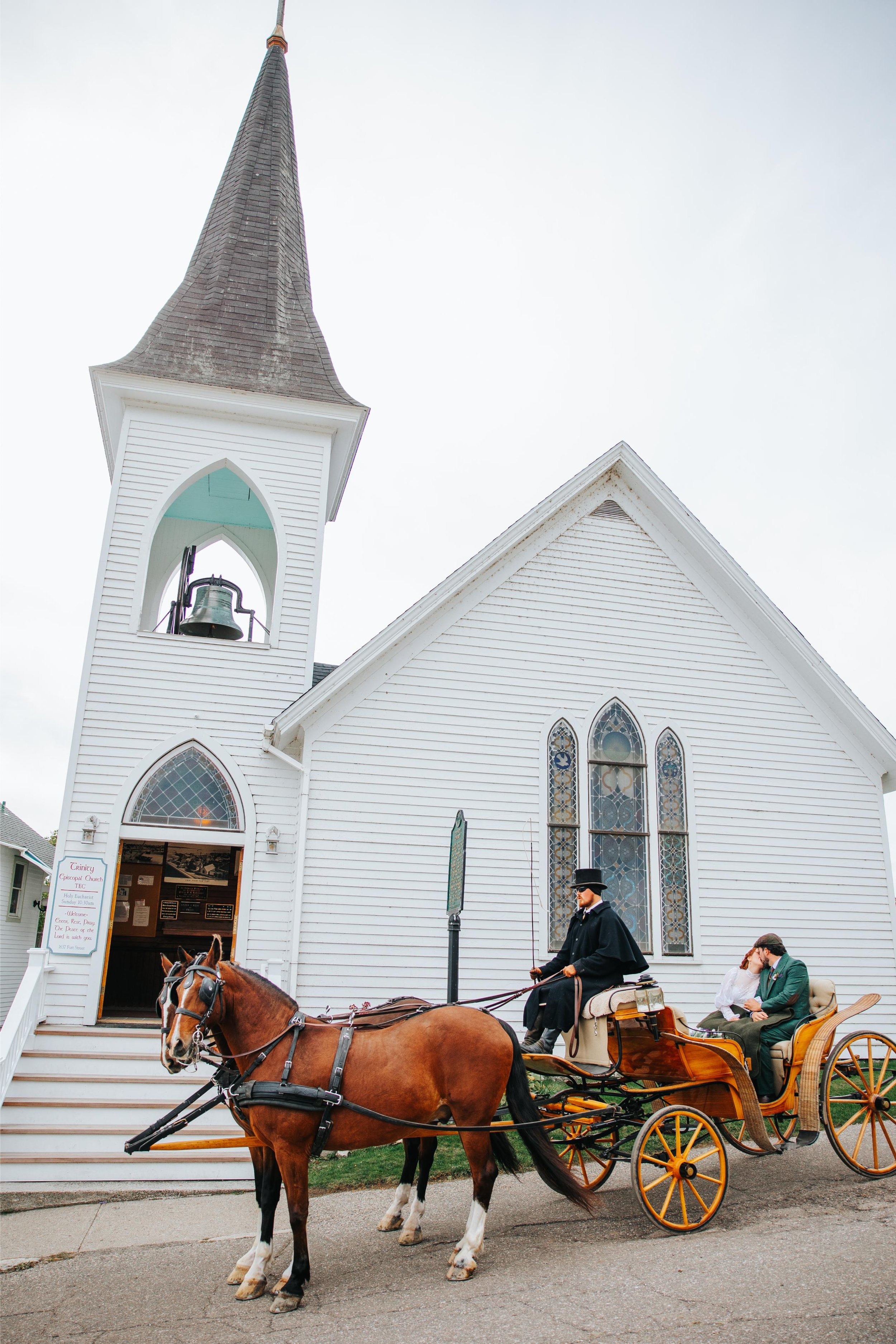 Trinity Episcopal Church (TEC) sign reading 'Holy Eucharist Sunday 10:30am' with a horse-drawn carriage in front