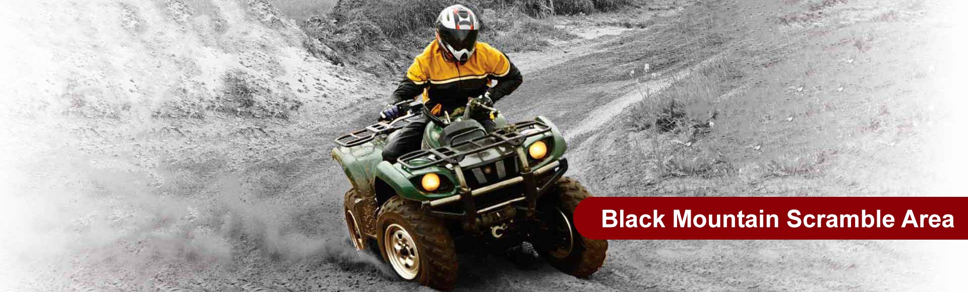 ATV rider in yellow jacket navigates a muddy off-road trail. Text reads: Black Mountain Scramble Area.