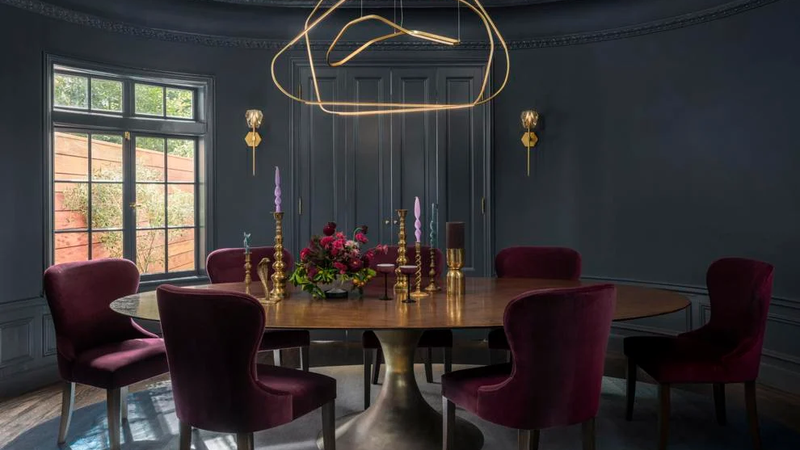 In the oval dining room nests a Julian Chichester table, custom Black Label Home chairs in Schumacher velvet and a custom rug by Ombre. The walls are painted Farrow and Ball’s Hague Blue, while the chandelier by Galerie Philia descends from a gold leaf painted ceiling by David Bonk.