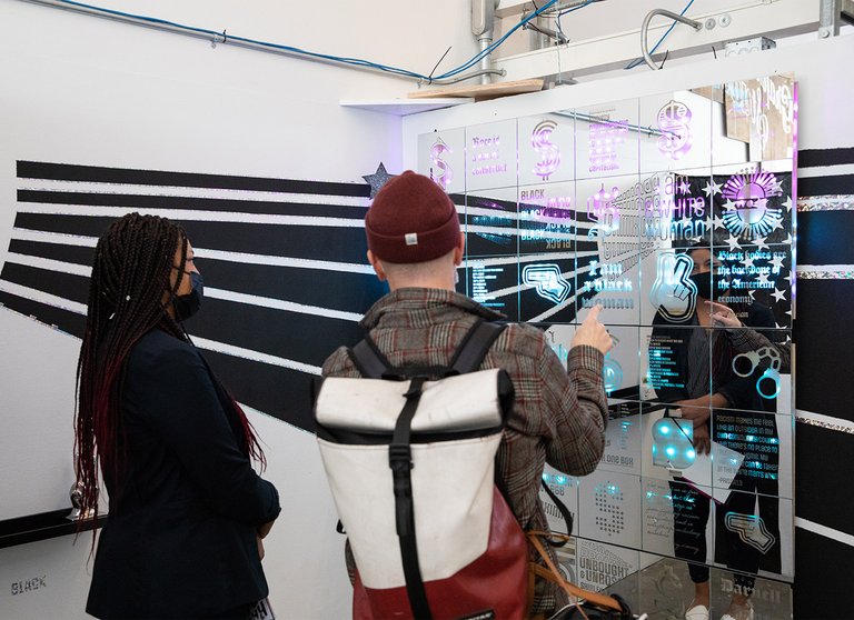 Two students looking into an artwork with text and images in purple and blue across a reflective surface.