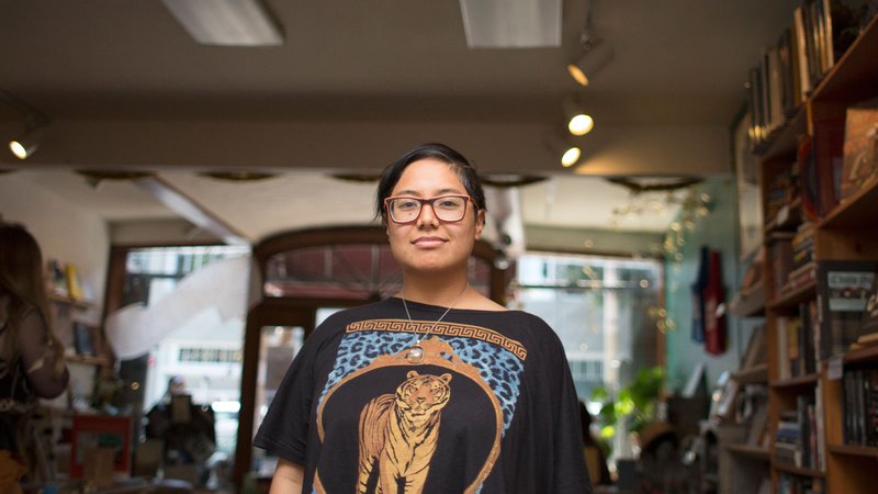 Dorothy Santos stands in the middle of a book shop with an archway above them, looking directly into the camera.