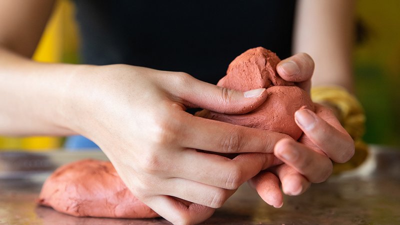 Close up image of a students hands sculpting red clay into a shape.