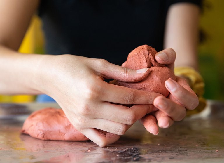 Close up image of a students hands sculpting red clay into a shape.