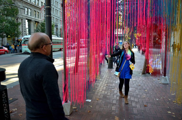 a woman walks through thousands of dangling neon strings on the street in San Francisco.