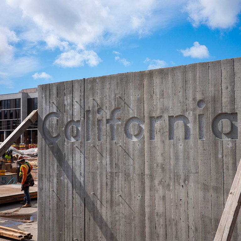 CCA Campus cast-in-place concrete sign visible while construction of building takes place in the background.