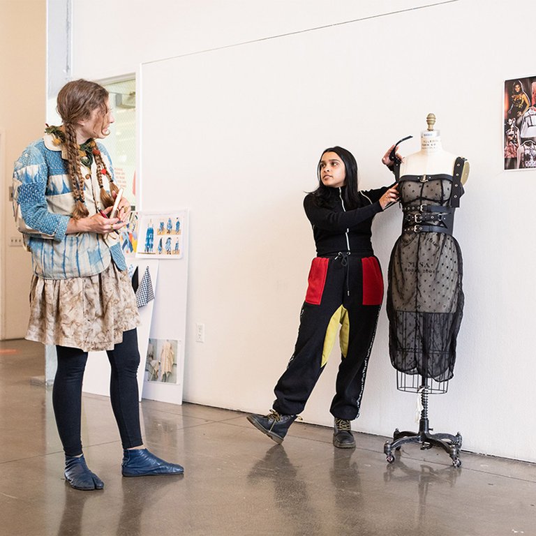 Fashion design student presenting their dress design to a colleague during a class.